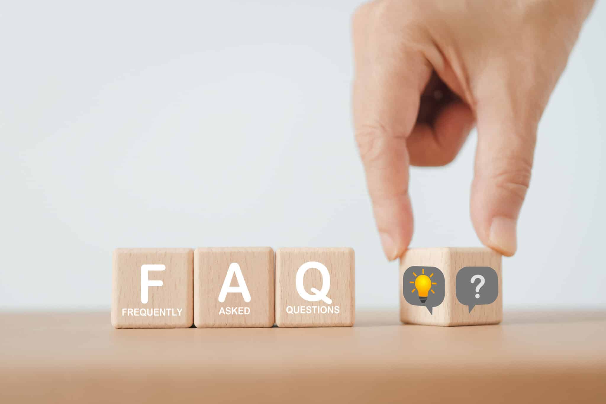 An image of a wooden cube block with "FAQ" written on it, with a hand flipping a question mark towards a lightbulb, FAQs About Surge Protection by Mister Sparky of Charleston
