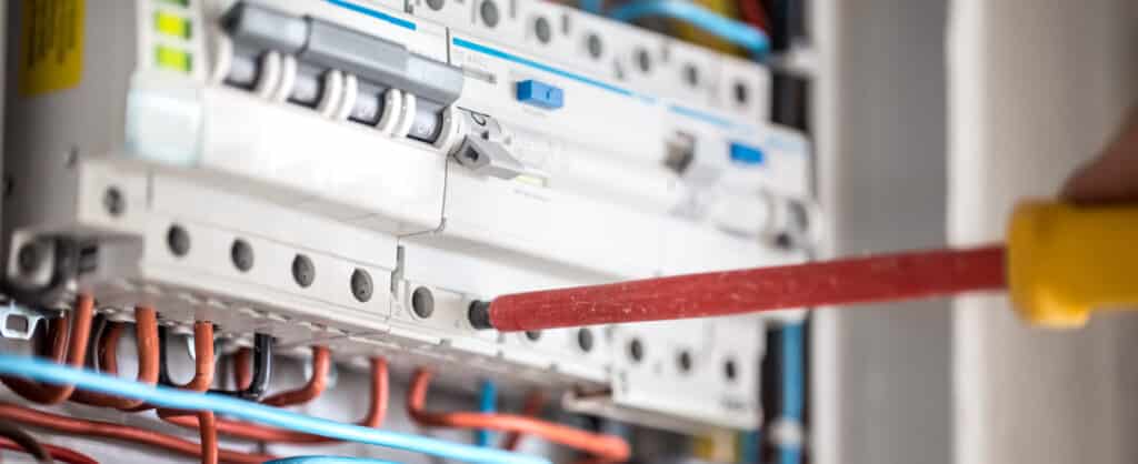 A male electrical technician working in a switchboard with fuses, performing installation and connection of electrical equipment.