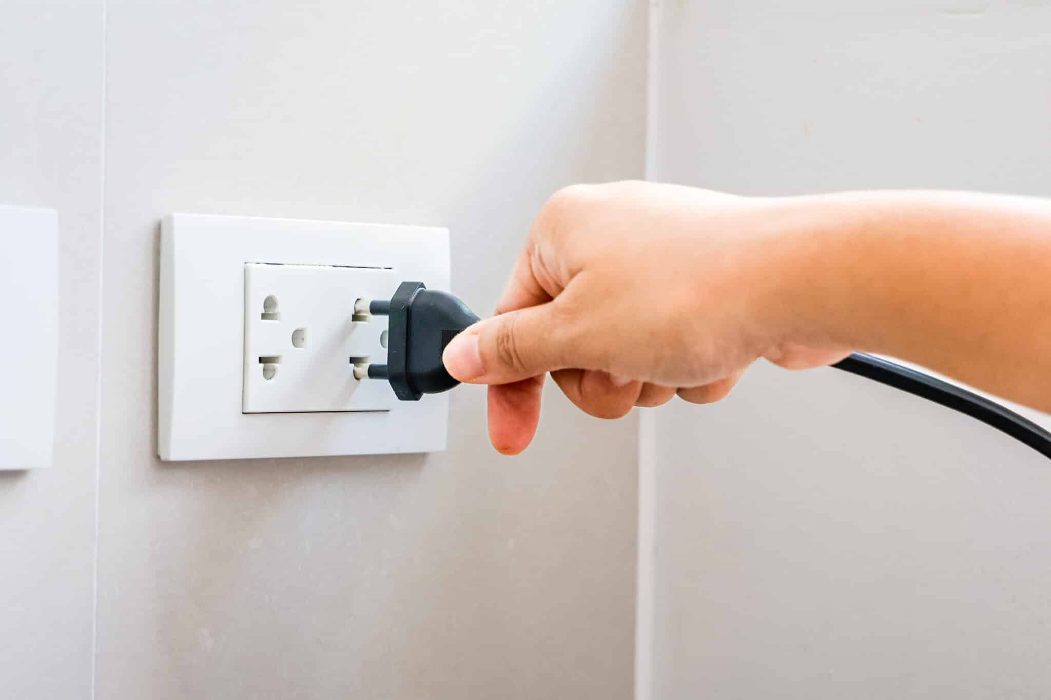 Hand holding a plug, connecting it to a tamper-resistant outlet on a wall.