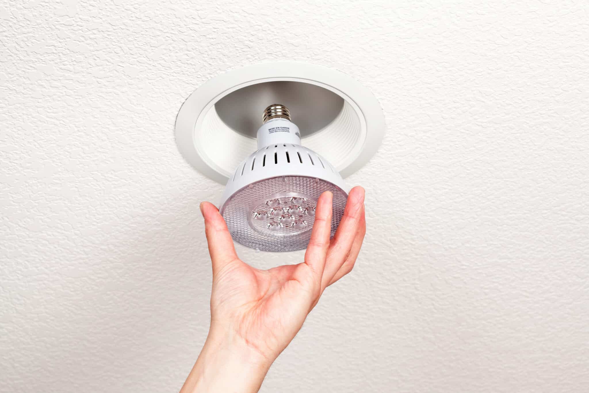 Hand Installing an IC-Rated LED Light Bulb into a Ceiling Fixture.