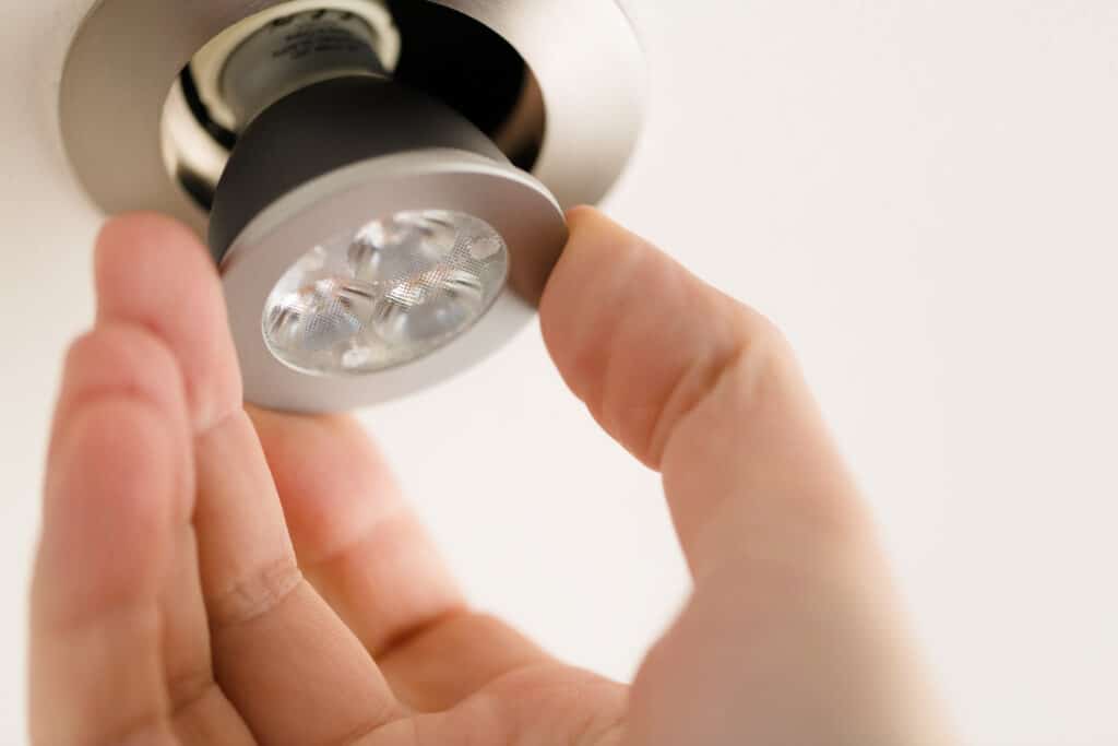 In lighting with IC ratings, a man is installing an LED light bulb into a ceiling can fixture.