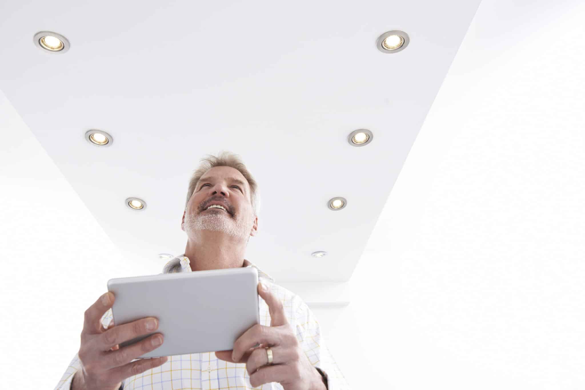 A man controlling smart home lighting with an app on a digital tablet.