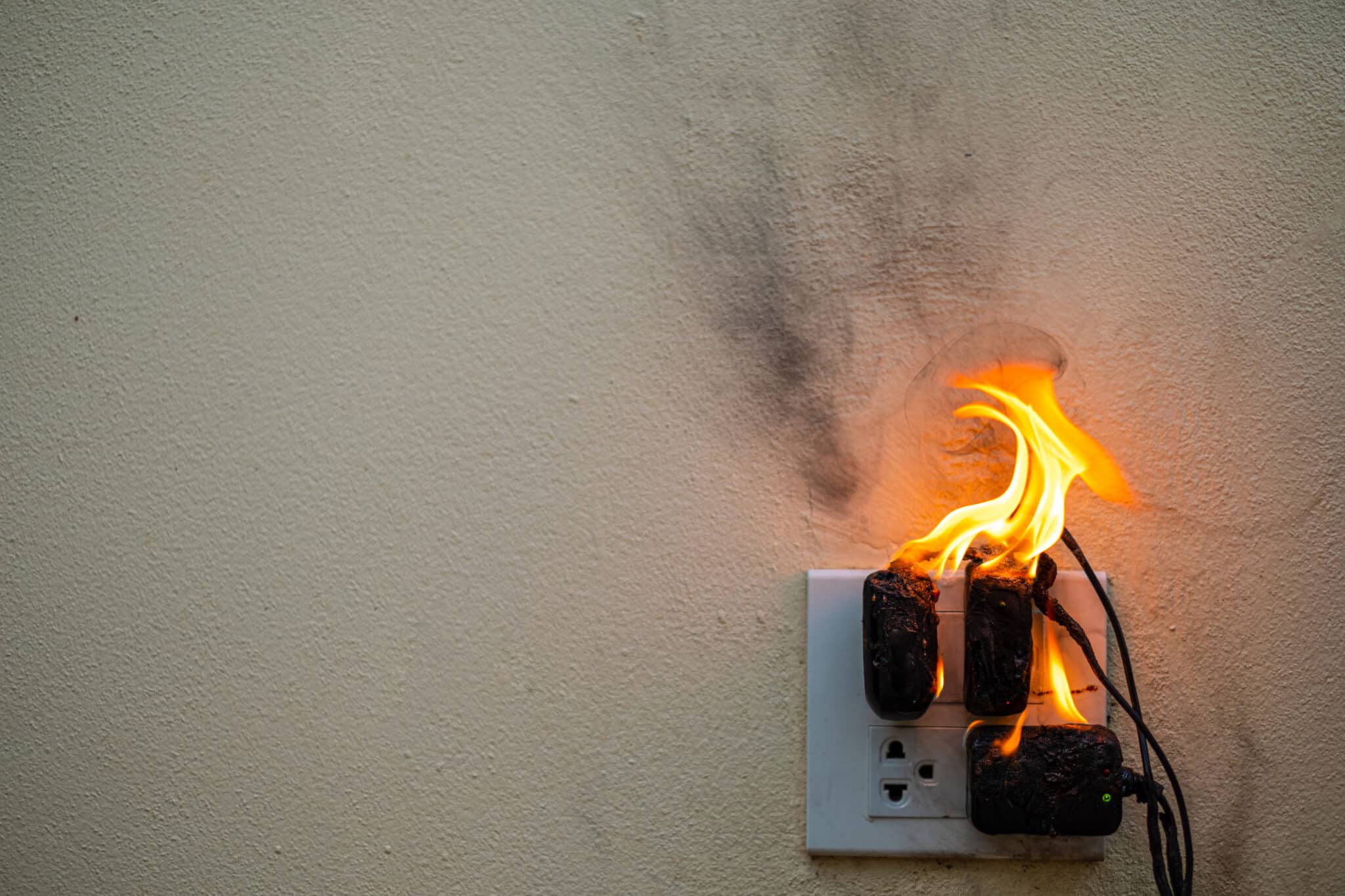 n adapter on fire at a plug receptacle on a white background, resulting in electrical overloads, a short circuit, and burnt electrical wires.