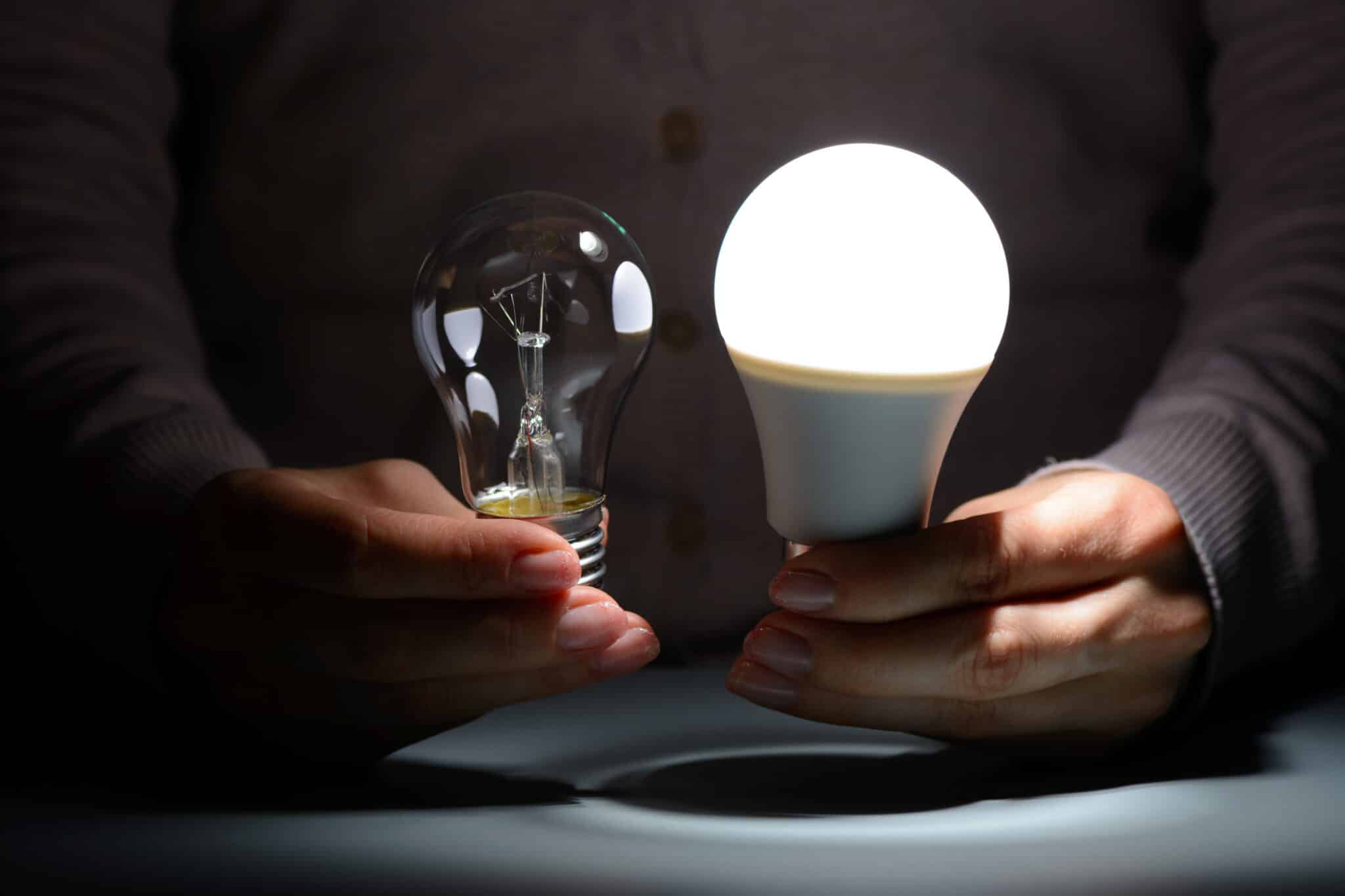 Hands holding energy-efficient LED and incandescent bulbs in the dark.